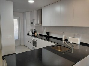 A modern kitchen with white cabinets, a black countertop, a stainless steel sink, a microwave, a coffee maker, and a toaster. - Modern apartment, sea view - 4 guests (San Juan de los Terreros)