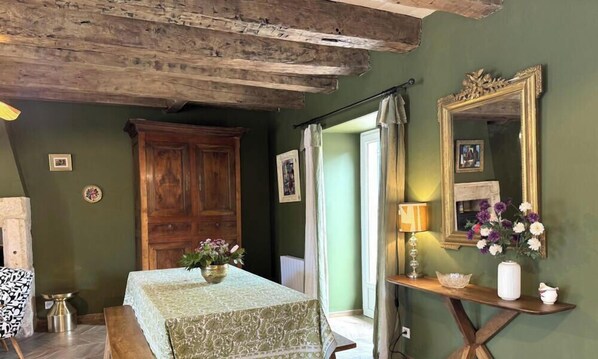 A room with a wooden ceiling, a table with a patterned tablecloth, a mirror, and a vase with flowers. - Stone house with parking - 4 guests (Blis-et-Born)