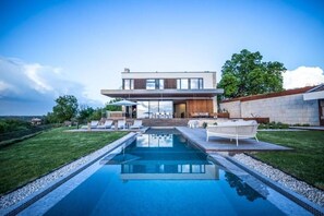 Ein modernes Haus mit Swimmingpool, Sitzgelegenheiten im Freien und Blick auf die Landschaft.