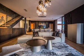 Ein modernes Wohnzimmer mit einer Couch, zwei Couchtischen, einer Treppe und einer Küche im Hintergrund.