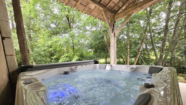 A hot tub with a logo, surrounded by trees, under a wooden structure. - Idyllic home, pets and parking - 6 guests (Saint-Vincent-Jalmoutiers)