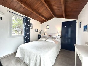 A bedroom with a bed, a desk, a window with curtains, a door, and a wall clock. - Quiet house, heated pool - 5 guests (Bretignolles-sur-Mer)