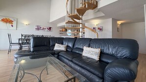 Ett modernt vardagsrum med en svart lädersoffa, ett soffbord i glas, en spiraltrappa och en matplats med ett svart metallbord och stolar.