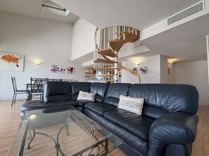 Ein modernes Wohnzimmer mit einem schwarzen Ledersofa, einem Glastisch, einer Wendeltreppe und einem Essbereich mit einem schwarzen Metalltisch und Stühlen.