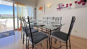 En matplats med ett glasbord och metallstolar, en skjutdörr i glas som leder ut till en uteplats och en väggmonterad lampa.