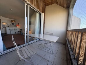 Ein Balkon mit einem weißen Tisch und Stühlen, eine Schiebetür zu einer Küche und ein Holzzaun.