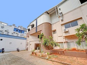 A building with a sign reading 'OYO TOWNHOUSE,' a paved entrance, and a small garden area with potted plants. - Collection O Yash Inn (Chennai)