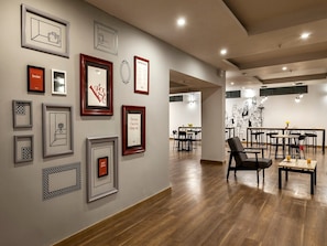 A modern interior with framed artwork on the walls, a dining area with tables and chairs, and a wooden floor. - Collection O Yash Inn (Chennai)