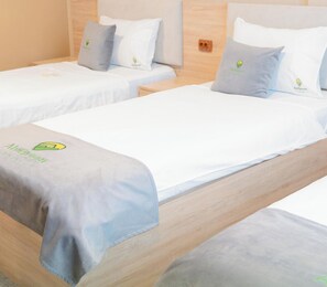 Two single beds with white linens and grey pillows, each bed has a grey blanket with the Abigreen logo.