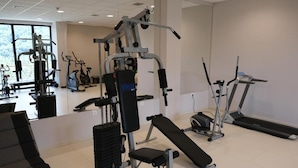Ein Fitnessstudio mit verschiedenen Trainingsgeräten, darunter eine Bank, Kraftgeräte und Laufbänder.