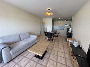 Ein kompakter Wohnbereich mit Sofa, Esstisch, Stühlen, Couchtisch, Küchenzeile mit Schränken und einer Pendelleuchte.