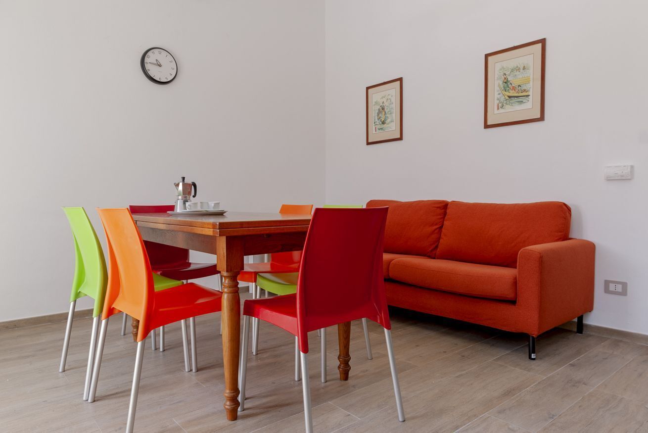 Ein Essbereich mit einem Holztisch, bunten Stühlen, einem roten Sofa und gerahmten Bildern an der Wand.