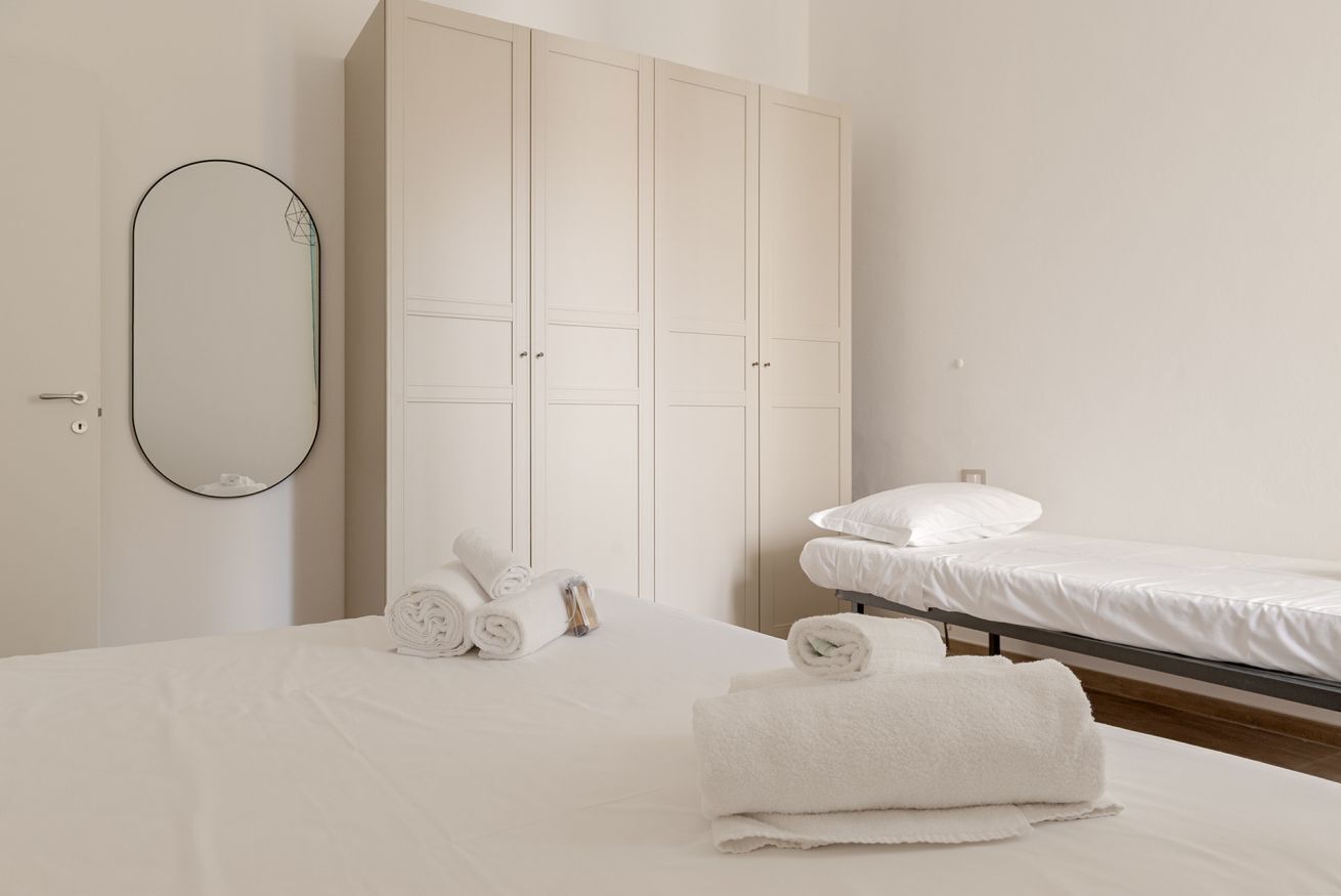 Een hotelkamer met een bed, een grote kledingkast, een spiegel en netjes gevouwen handdoeken.
