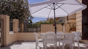 Un pati amb taula i cadires, una ombrel·la blanca i una porta.