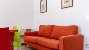 Habitació amb un sofà, una taula de dinar amb caires i dos quadres al mur.