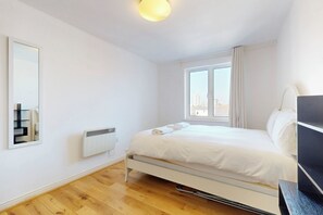 Ein Schlafzimmer mit Bett, Fenster, Heizkörper und Spiegel.