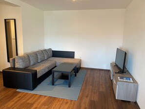 Ein modernes Wohnzimmer mit einem Ecksofa, einem Couchtisch, einem Flachbildfernseher und Holzboden.