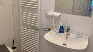 A bathroom with a white toilet, a sink with a mirror above it, and a towel rack. - Fischerspfad (Norden)