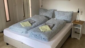A bedroom with a bed, bedside tables, a shelf, and a door. - Fischerspfad (Norden)