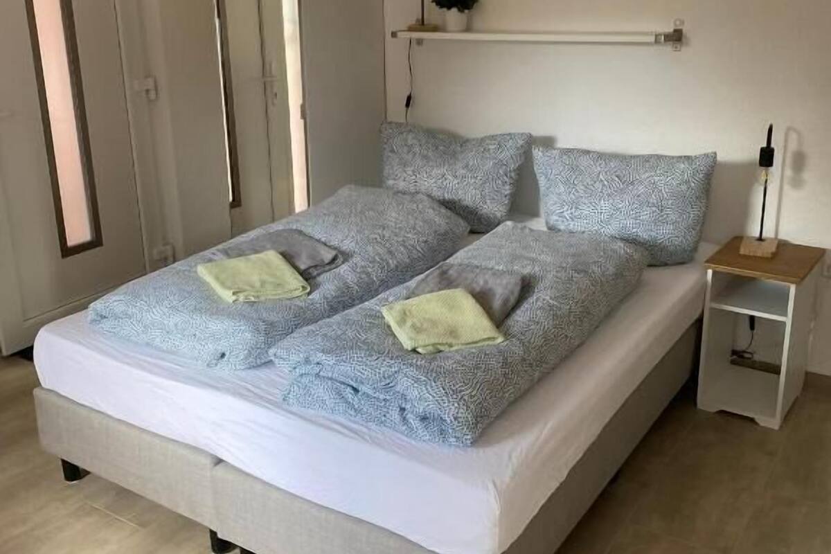 Un dormitorio con cama, mesitas de noche, una estantería y una puerta.