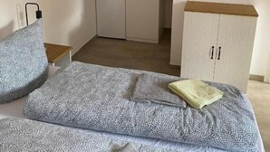 A bedroom with a bed, pillows, a bedside table, a wardrobe, and a kitchen area in the background. - Fischerspfad (Norden)