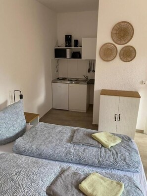 Makuuhuone, jossa on sänky, tyynyjä, yöpöytä, vaatekaappi ja taustalla näkyy keittiönurkkaus.