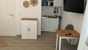 A compact living space with a kitchenette, a dining area, and a TV mounted on the wall. - Fischerspfad (Norden)