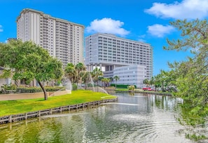A high-rise hotel with a water feature in front, surrounded by greenery and a clear sky. - North Hampton 901 Oceanfront in/out pool/Beach (Myrtle Beach)