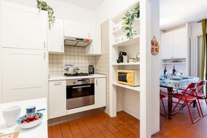 A compact kitchen with white cabinets, a stove, oven, and a microwave. There is a dining area with a table and chairs. - GuestHost - La Pineta Charming Home in Tirrenia (Tirrenia)