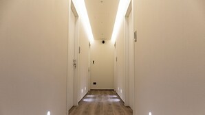 Un pasillo largo y estrecho con paredes blancas y suelo de madera, que conduce a una puerta al final.