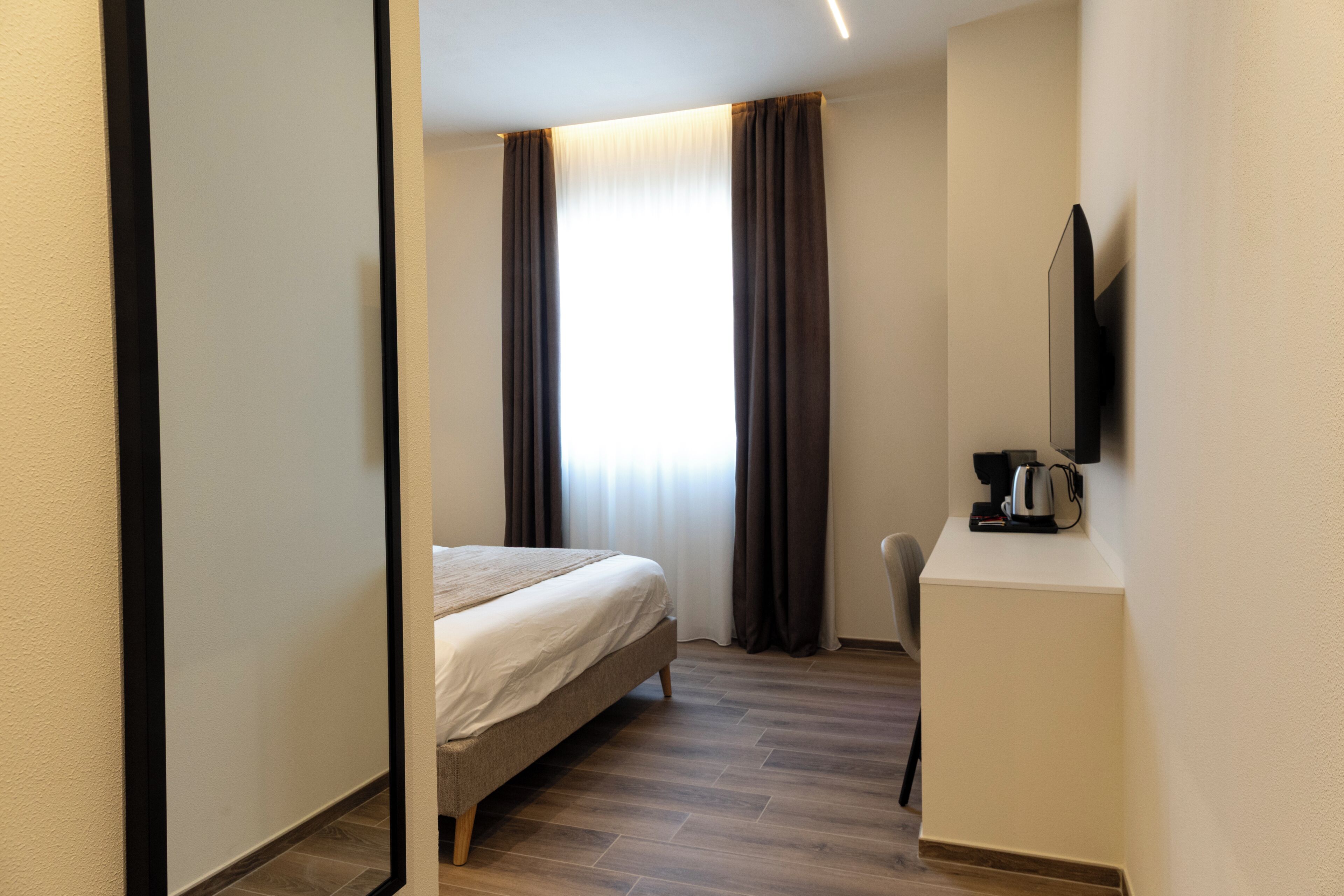 A hotel room with a bed, a coffee machine, a TV, and a window with curtains.