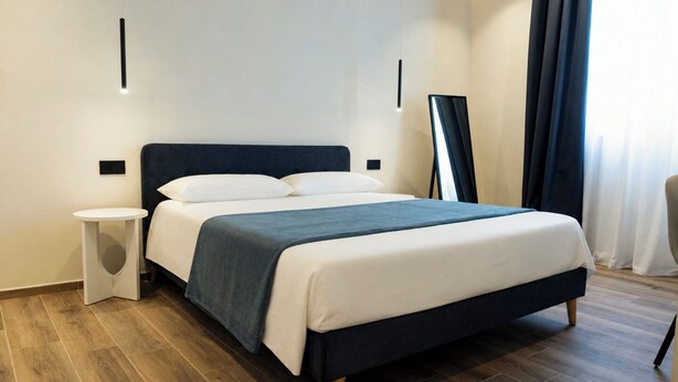 Una habitación de hotel moderna con cama, mesita de noche y espejo en la pared.