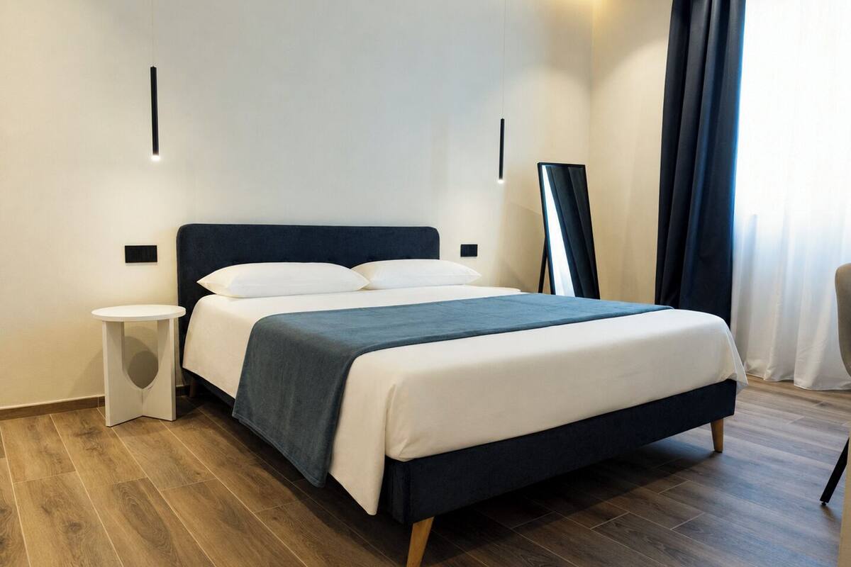 Una habitación de hotel moderna con cama, mesita de noche y espejo en la pared.