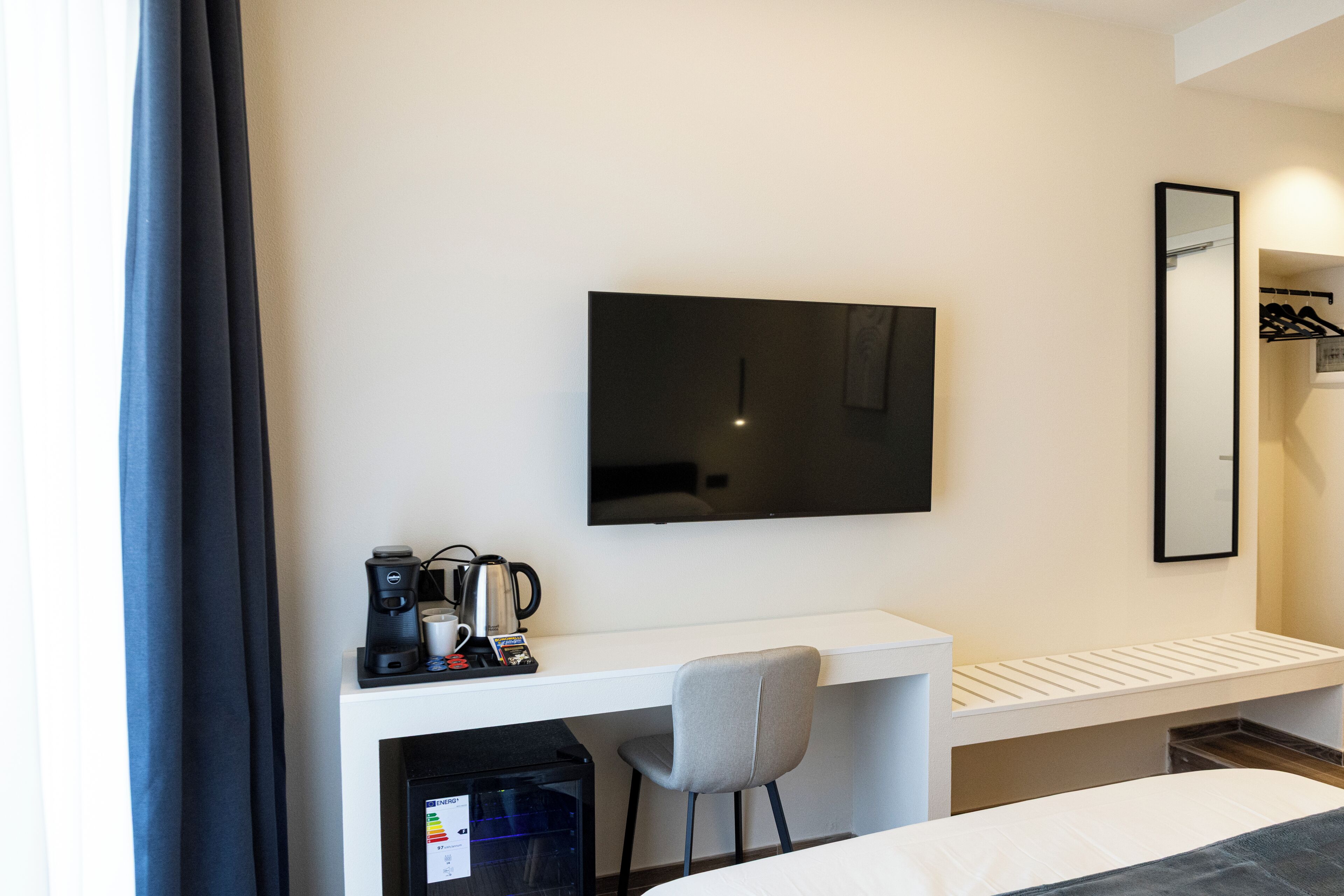 Une chambre d’hôtel comprenant un lit, un bureau avec une chaise, un téléviseur à écran plat, une machine à café et un miroir.
