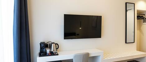 Une chambre d’hôtel comprenant un lit, un bureau avec une chaise, un téléviseur à écran plat, une machine à café et un miroir.