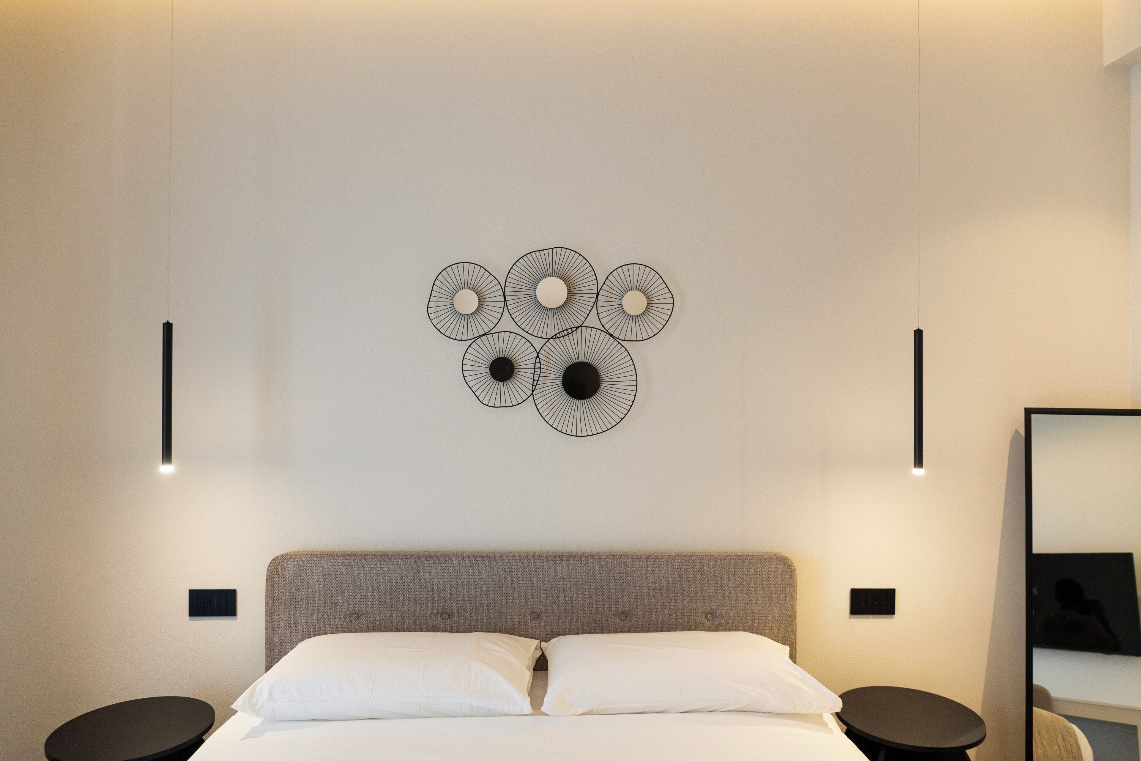 A modern hotel room with a bed, a wall-mounted light fixture, and a decorative wall art piece.