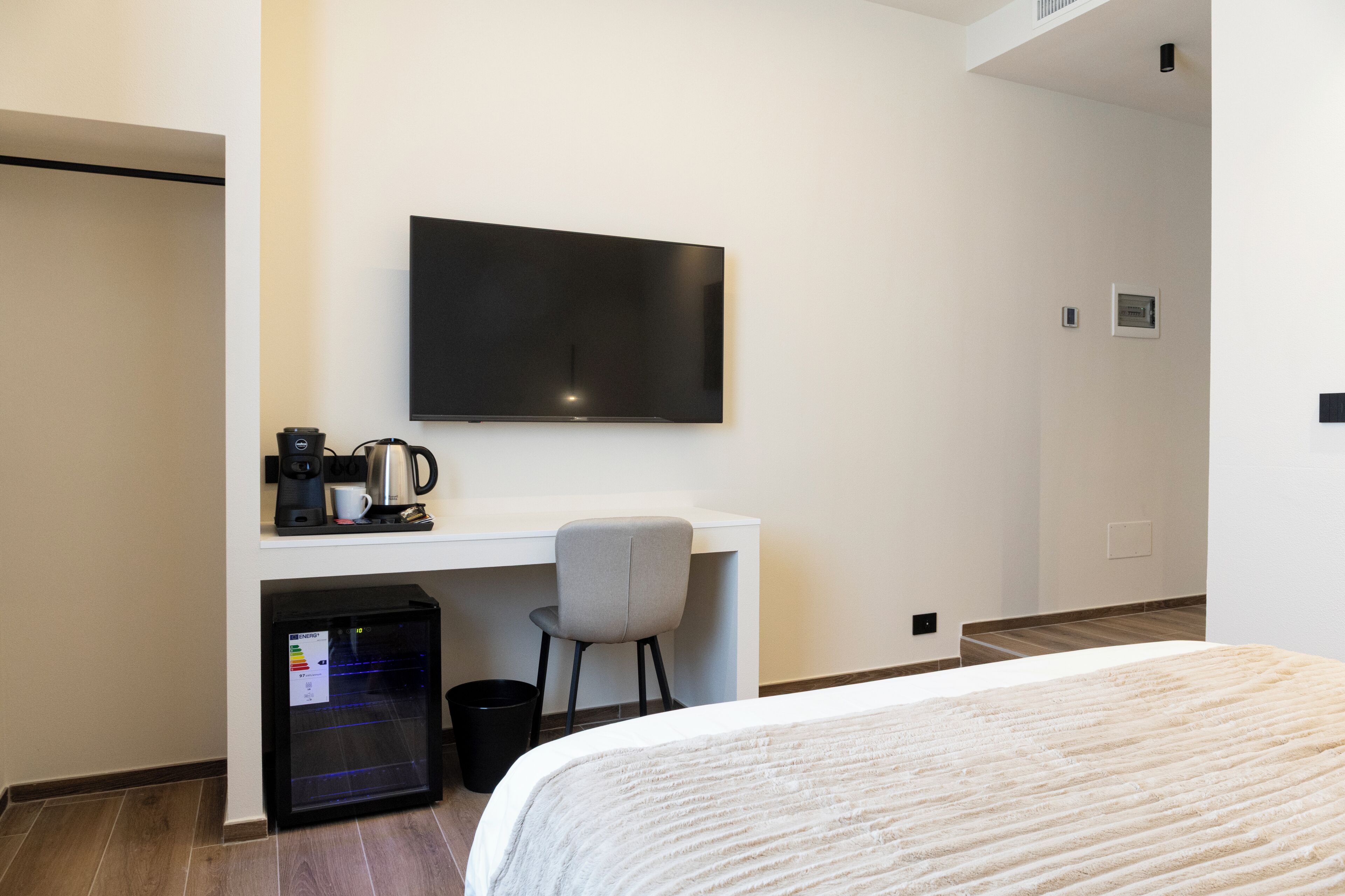 A hotel room with a bed, a desk with a chair, a coffee maker, a television, and a mini-fridge.