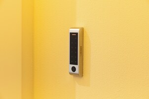 Una tastiera elettronica fissata al muro, probabilmente per una serratura, su una parete gialla con superficie strutturata.