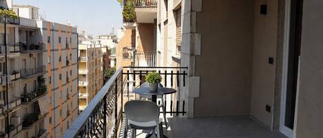 A balcony with a table and chairs, a potted plant, and a view of neighboring buildings.