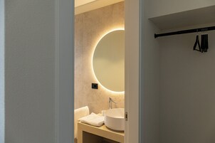 Un bagno con uno specchio rotondo, un lavandino e un portascopevoli.