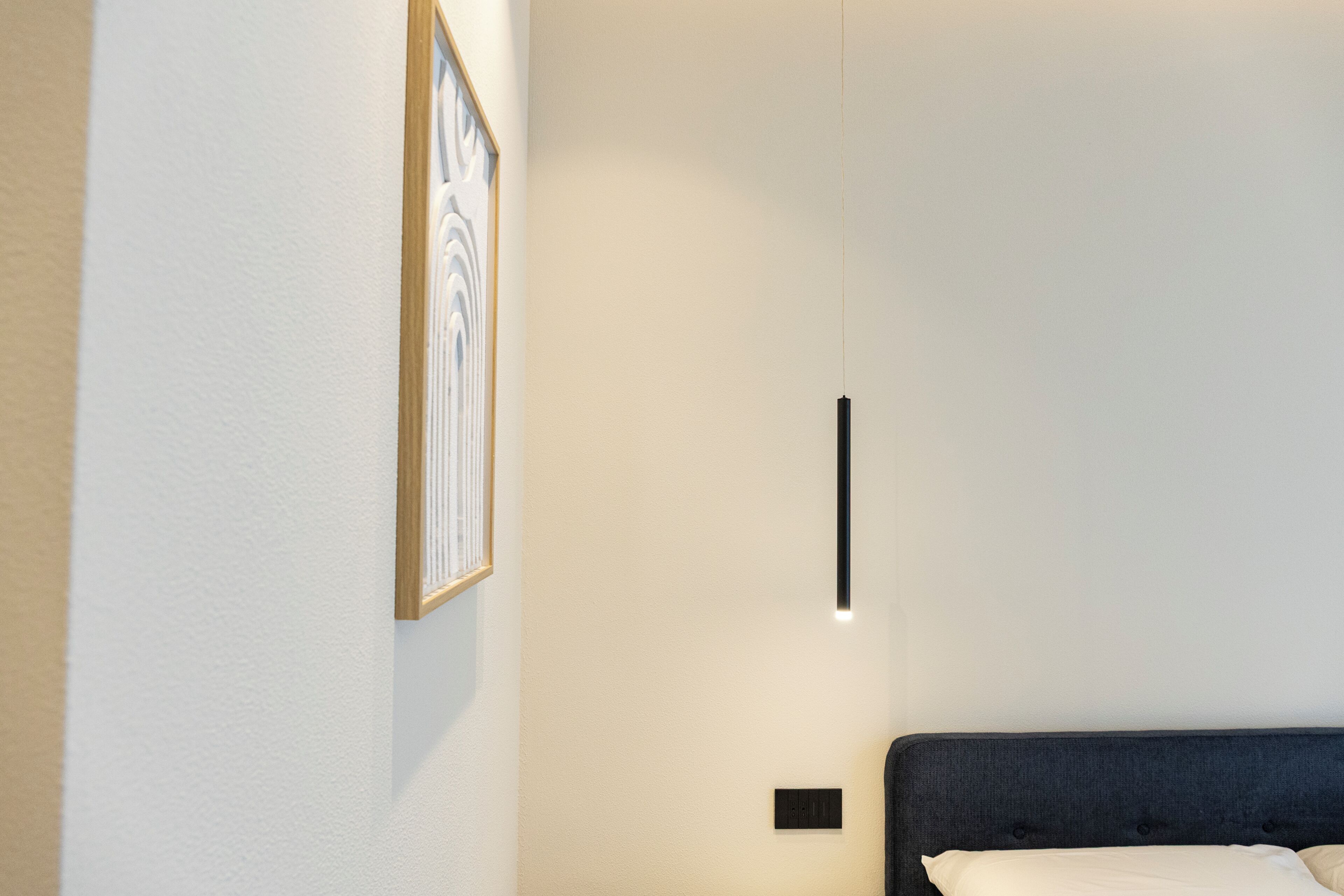 Une chambre à coucher avec un lit, une lampe fixée au mur et un tableau encadré.