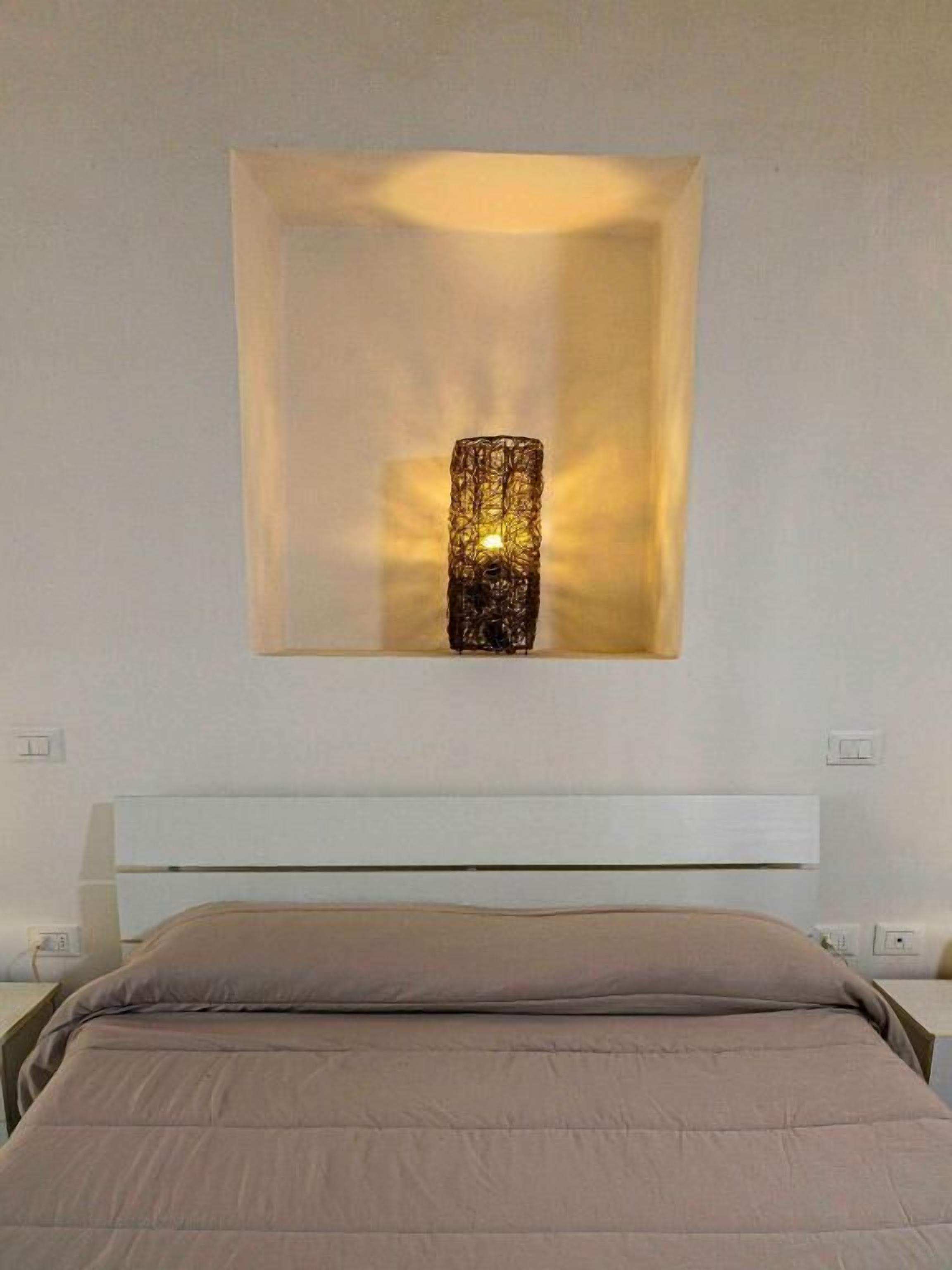 A bed with a headboard, a wall-mounted light fixture, and a power outlet.