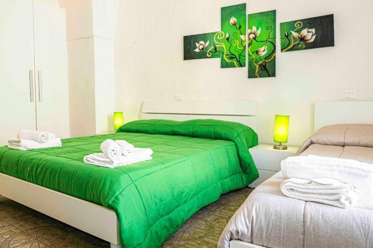 Habitación de hotel con dos camas, ropa de cama verde y beige, toallas blancas, un armario blanco y una pared con tres cuadros.