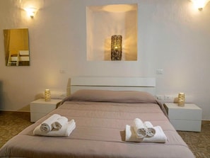 A hotel room with a bed, two bedside tables, a wall-mounted light fixture, and a mirror.
