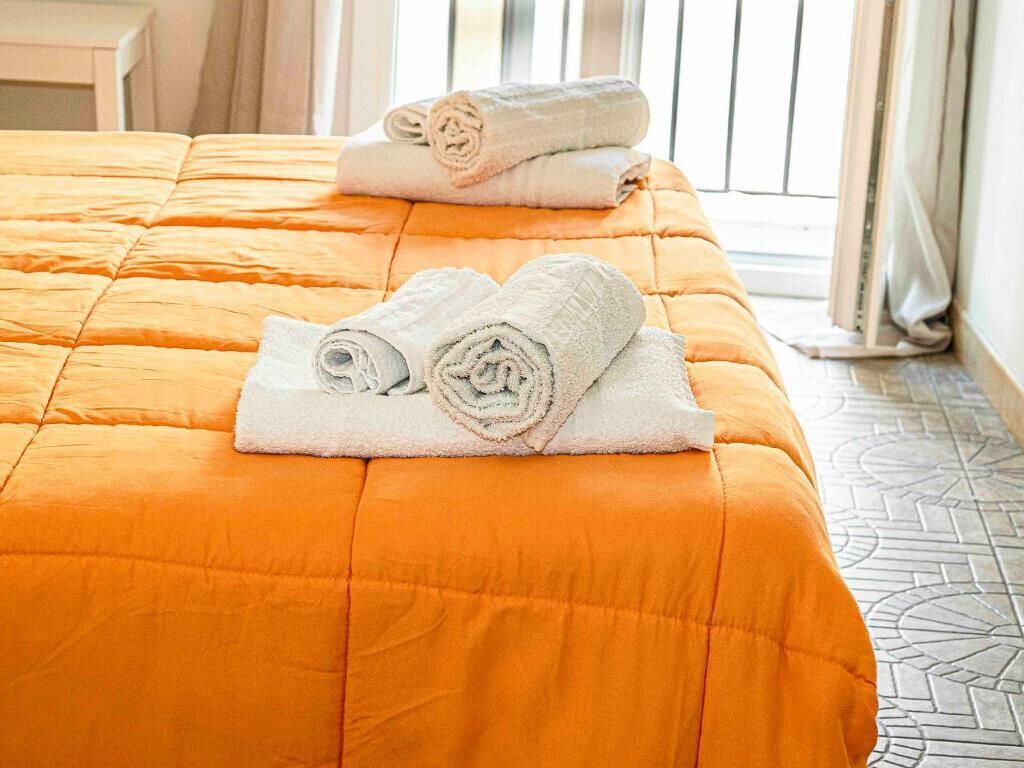 A bed with an orange quilt and two rolled white towels.