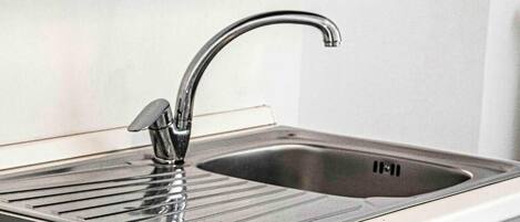 A kitchen with a stainless steel sink, a black countertop, and a white backsplash.