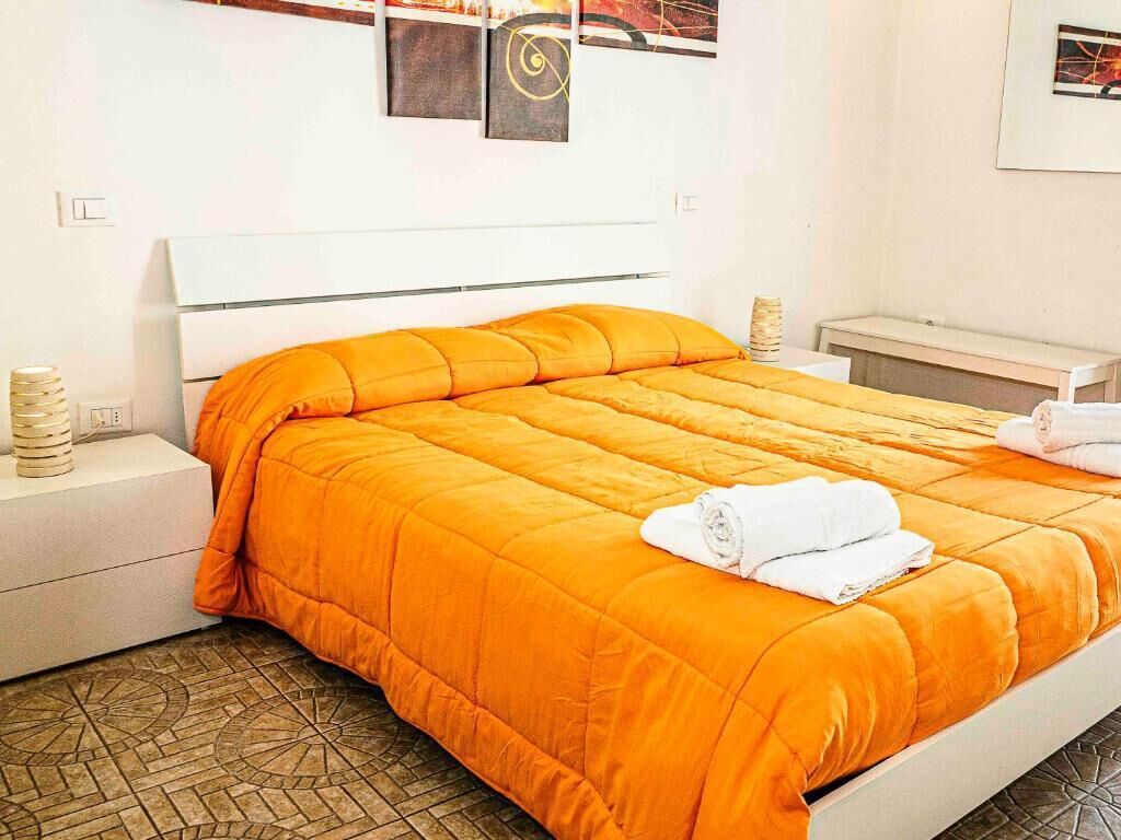 A hotel room with a bed, a bedside table, a nightstand, and a wall-mounted artwork.