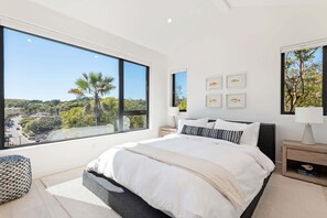 Ein Schlafzimmer mit großem Fenster, einem Bett, Nachttischen und Wandbildern.