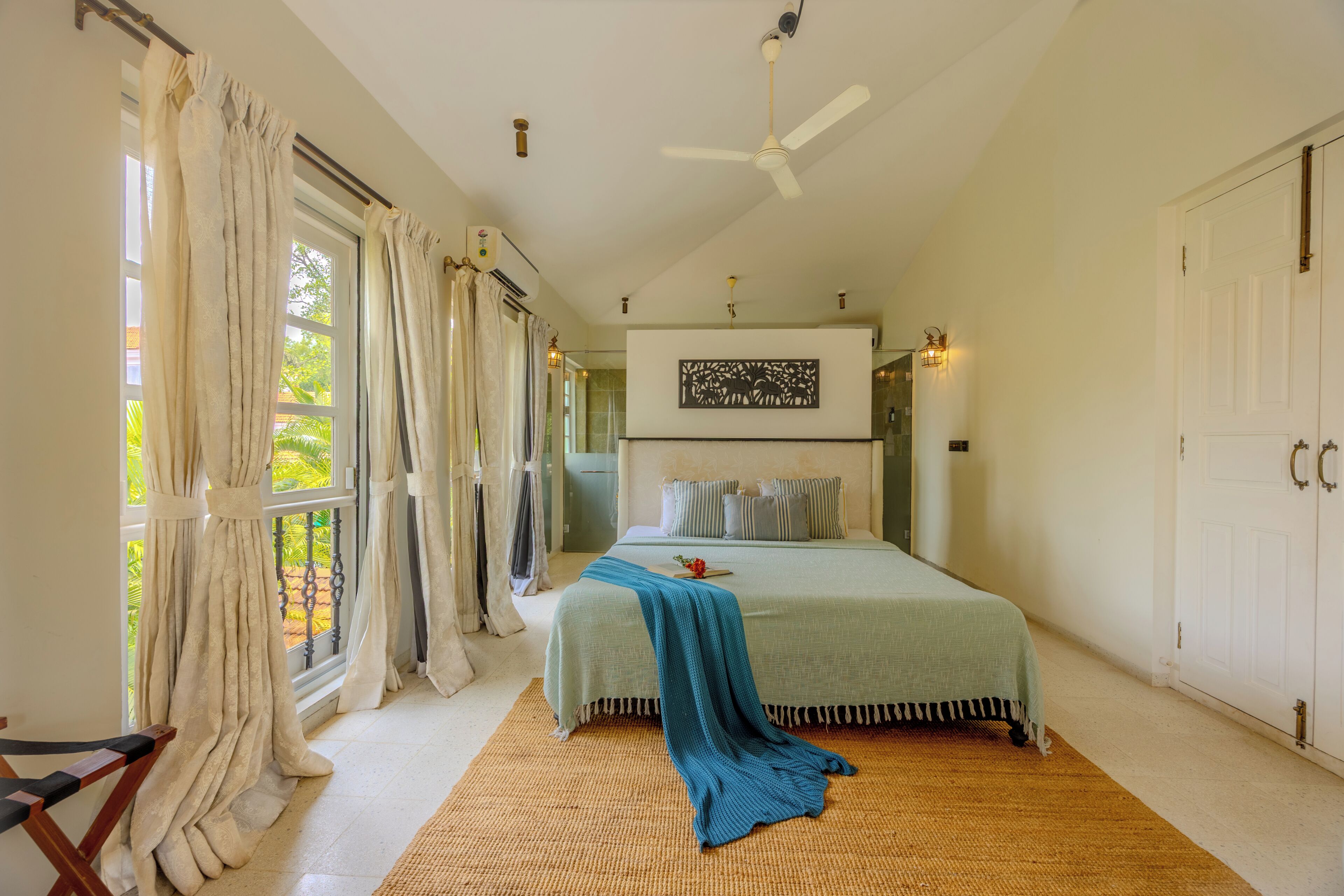 Ein Schlafzimmer mit Bett, Vorhängen, Deckenventilator, Wandbild und Fenster mit Vorhängen.