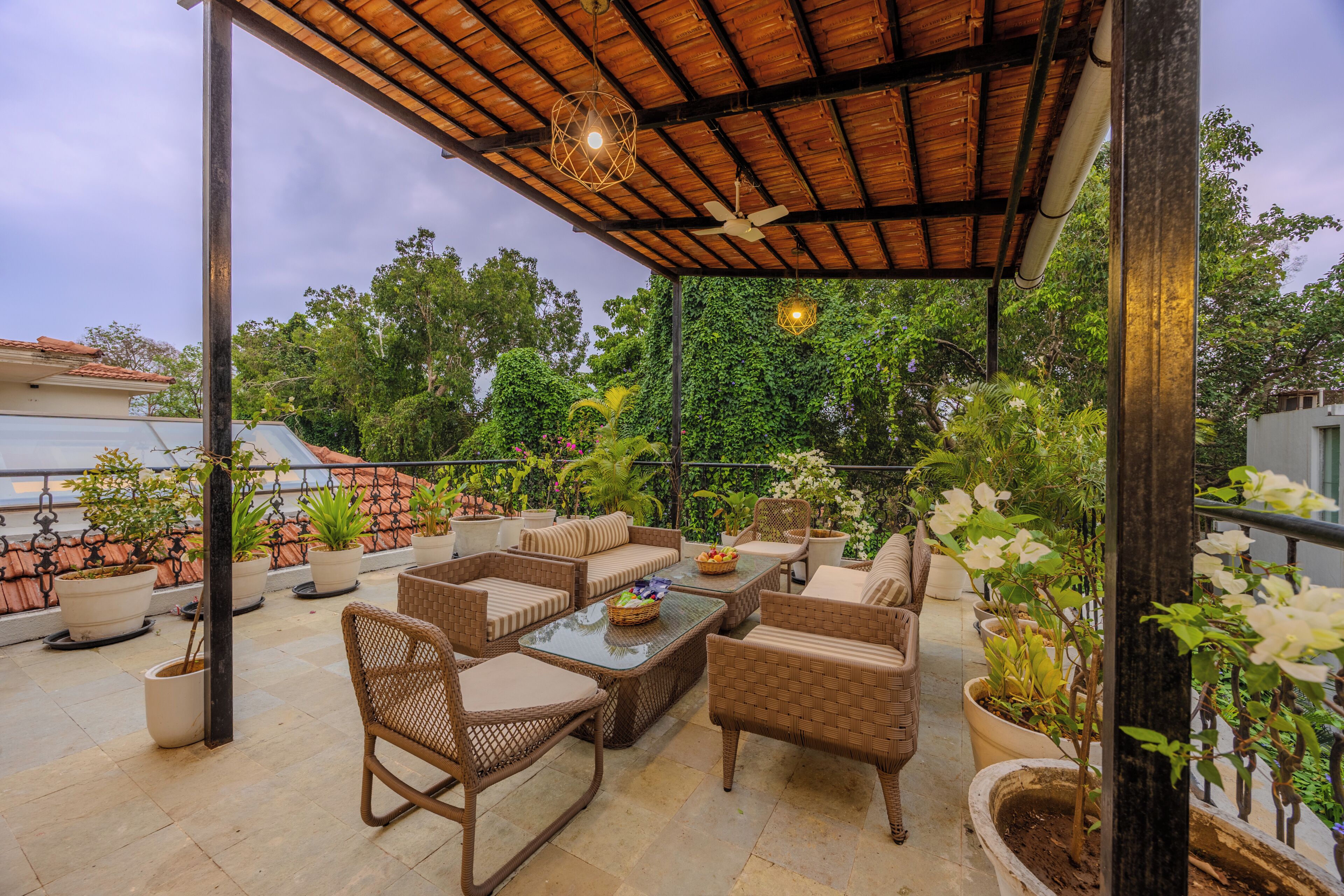 Une terrasse extérieure aménagée avec des meubles en osier, des plantes en pot et un ventilateur de plafond.
